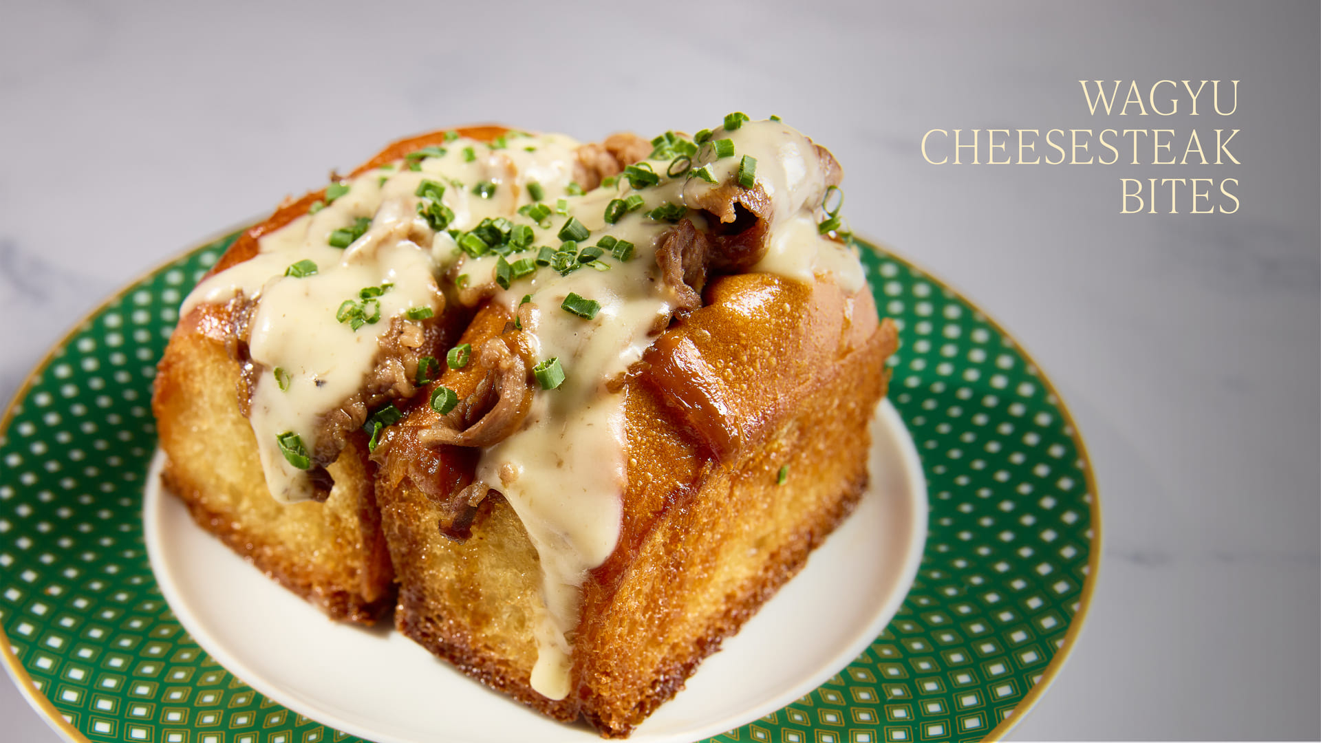 Wagyu cheesesteak bites topped with melted cheese and chives on a plate