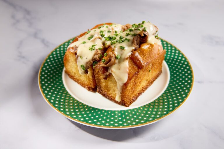 Toasted milk bread topped with wagyu beef, melted cheese sauce, and chives on a decorative plate.