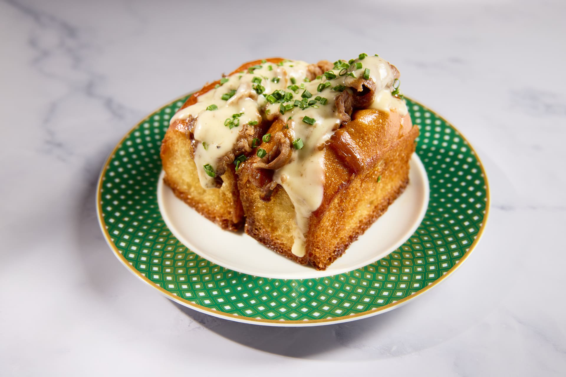 Toasted milk bread topped with wagyu beef, melted cheese sauce, and chives on a decorative plate.