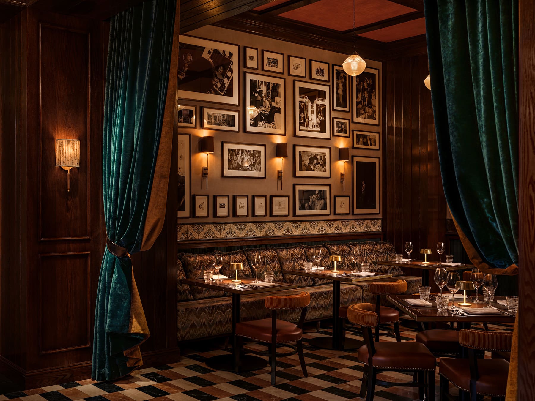 Intimate restaurant booth seating with framed photographs, velvet curtains, and candlelit tables.