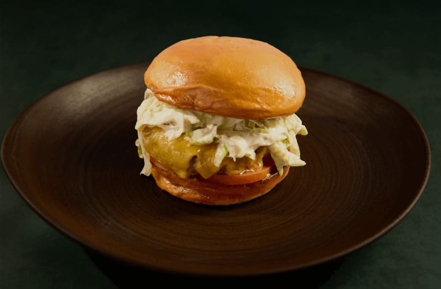 Cheeseburger with melted cheese, coleslaw, and tomato on a toasted bun, served on a dark plate