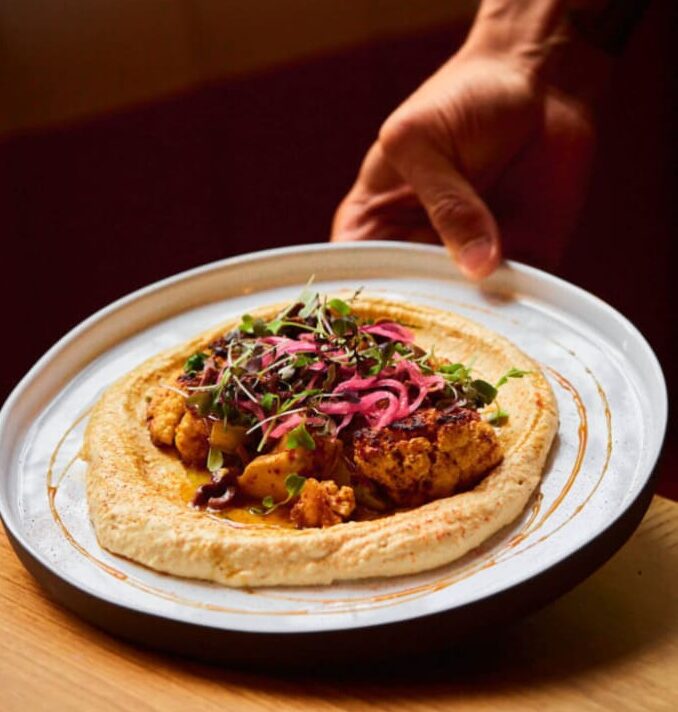 Plated entrée served over hummus topped with pickled onions and microgreens
