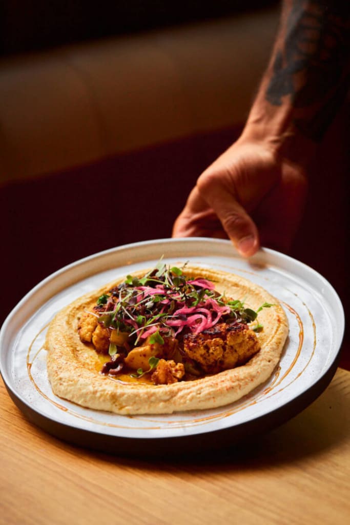 Plated entrée served over hummus topped with pickled onions and microgreens
