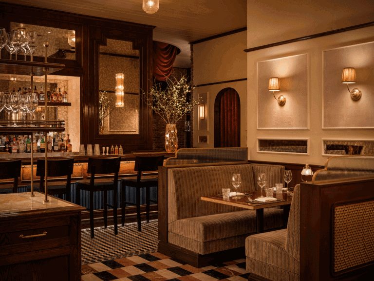 Elegant restaurant interior featuring a polished bar, upholstered booth seating, marble-topped tables, warm ambient lighting, and refined décor in a contemporary dining space.